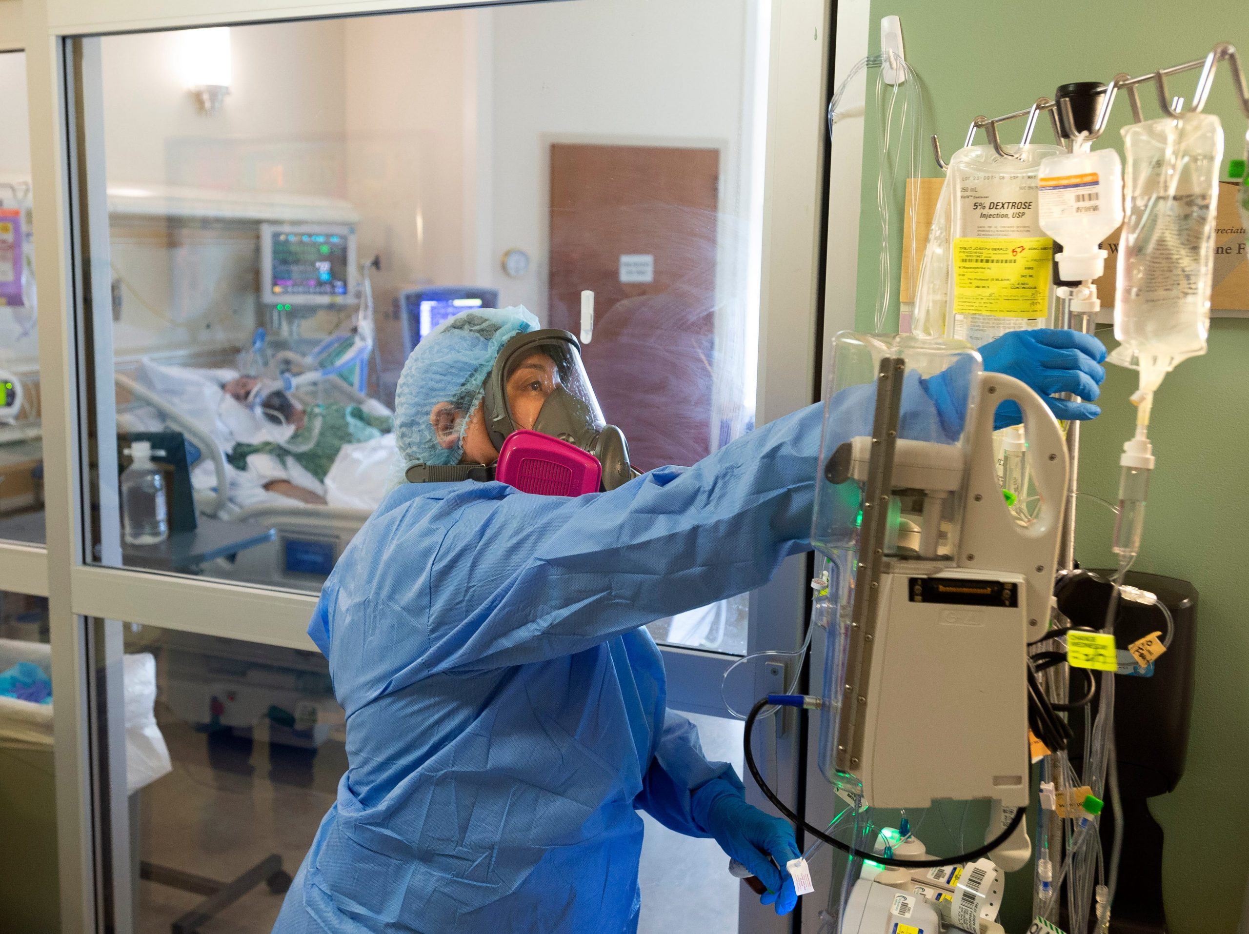 A nurse dressed in PPE tends to medical equipment in a hospital