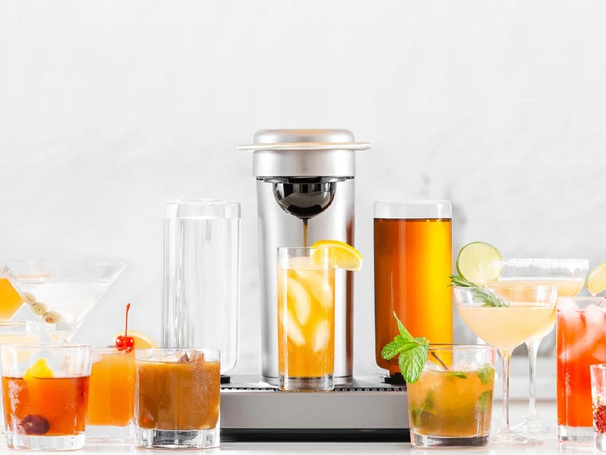 A small, shiny cocktail maker and various colorful cocktails around the machine