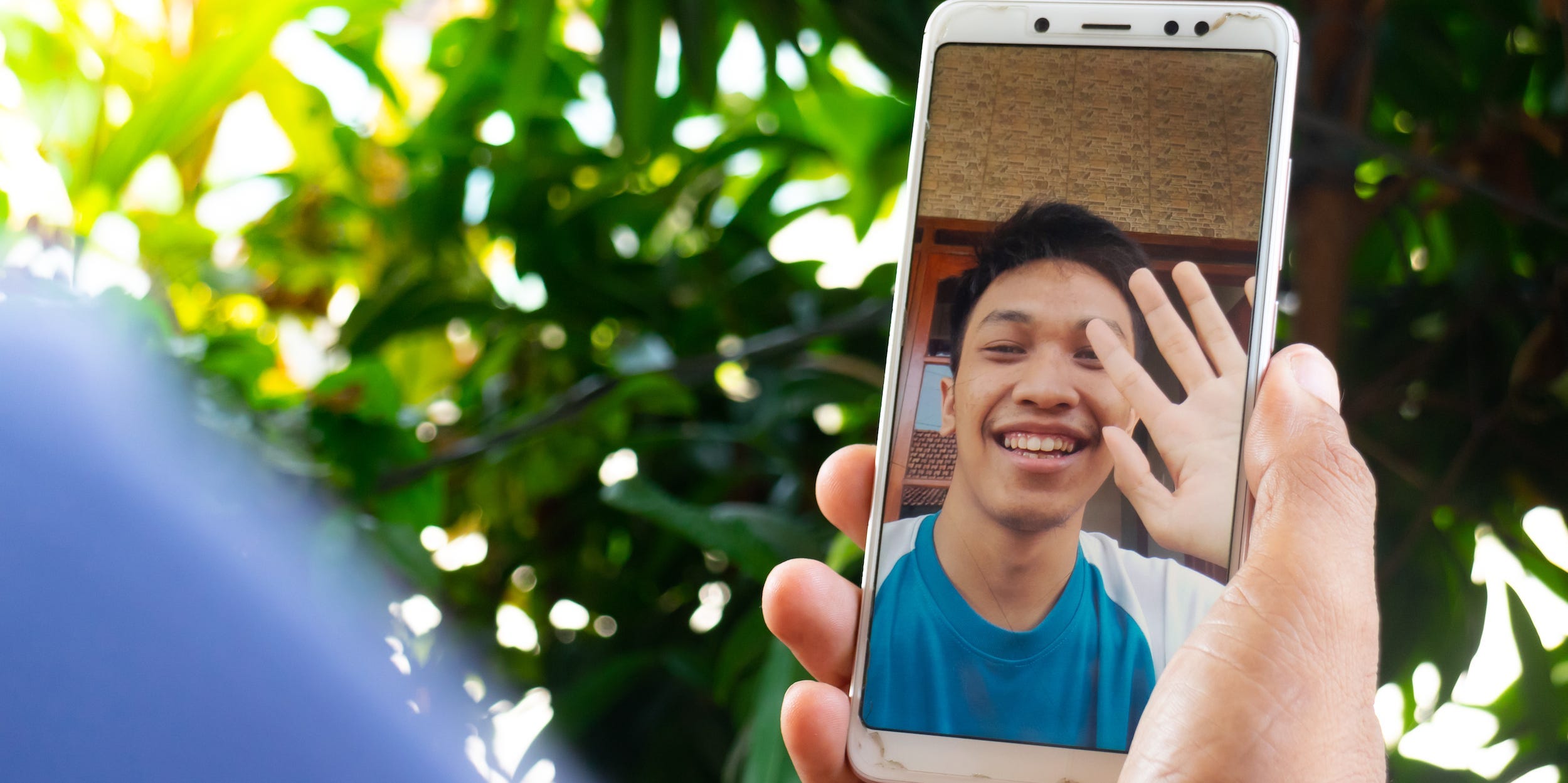 Close-up of a video chat call on a smartphone, person waving hello
