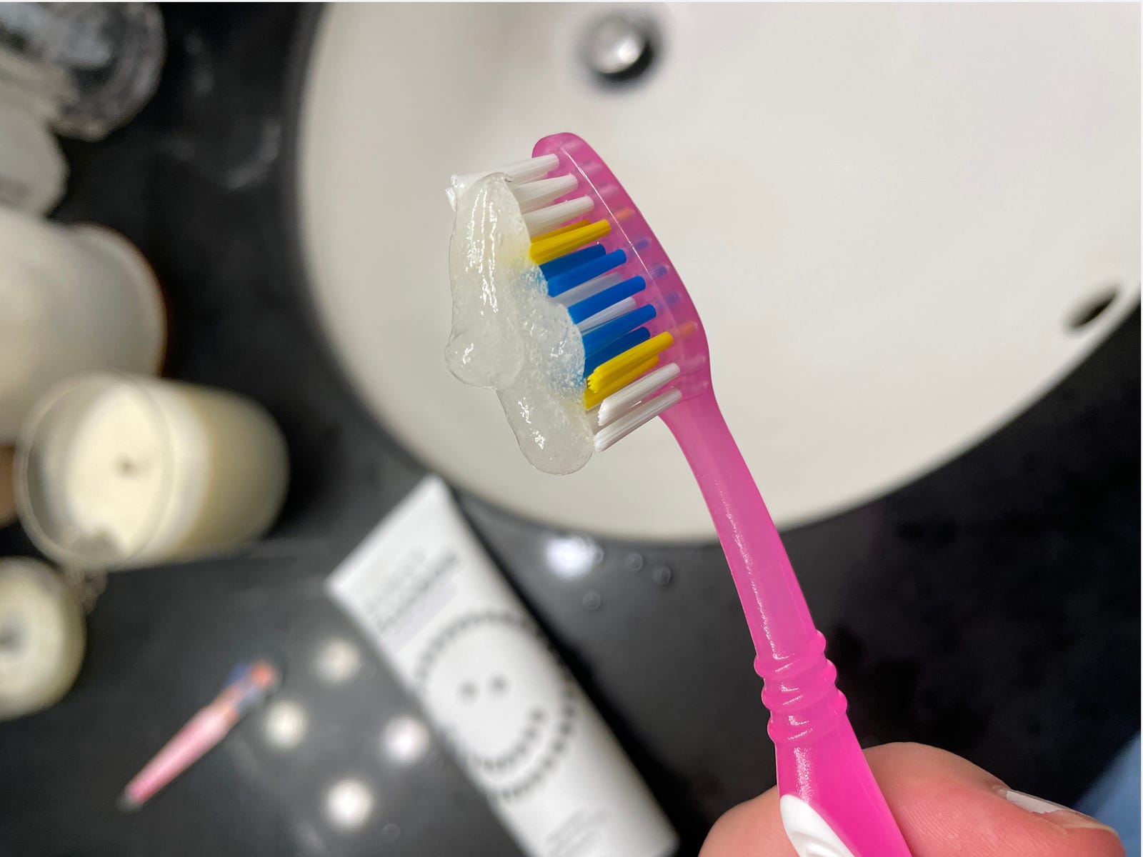 A pink toothbrush over a bathroom sink with toothpaste on it
