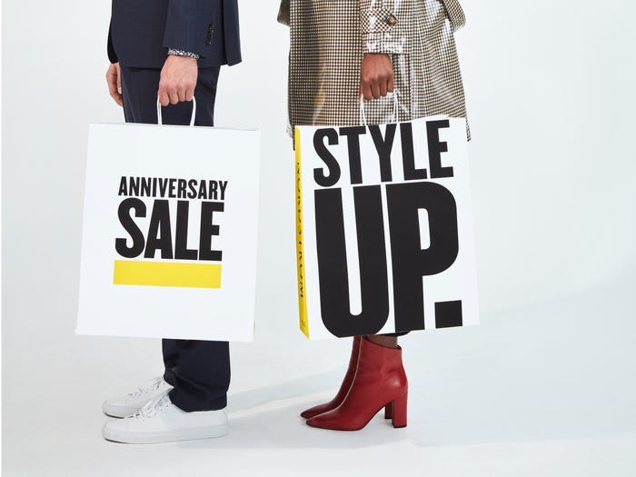 Masculine person on the left and feminine person on the right, each holding a Nordstrom Anniversary Sale bag in hand.