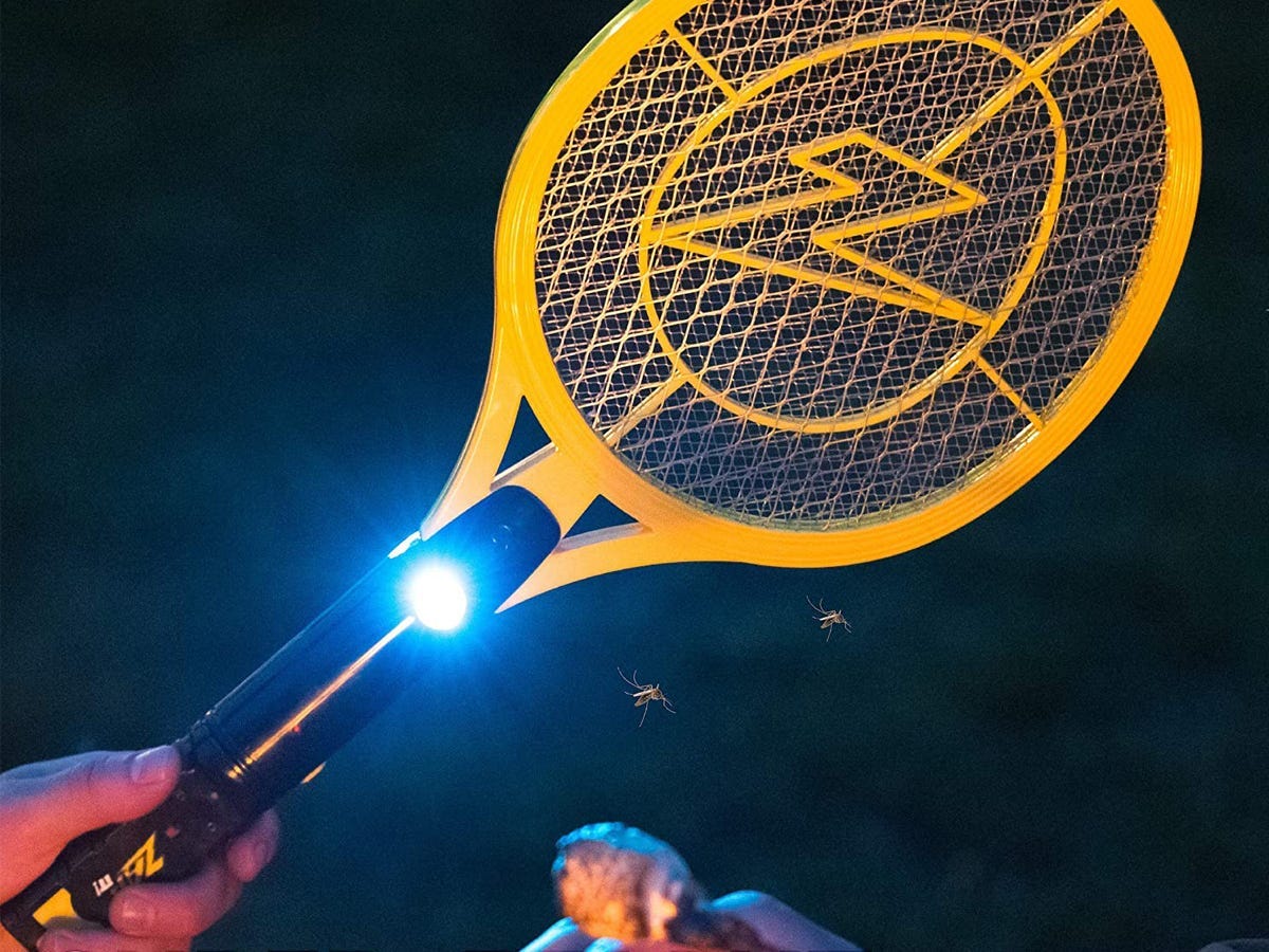 A hand holding a Zap It Bug Zapper at a campfire with s'mores