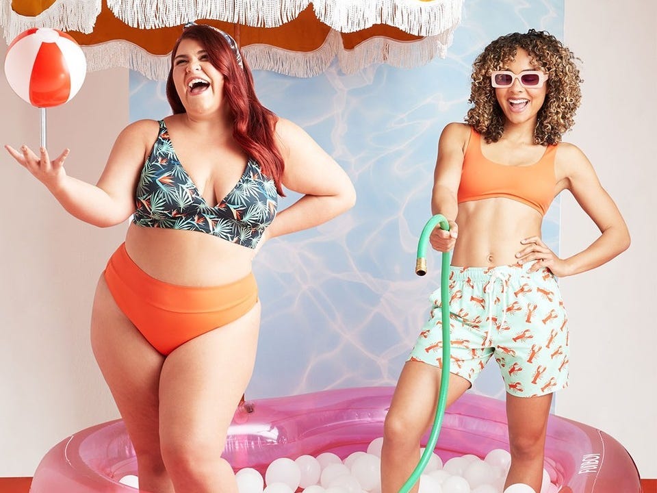 Two feminine persons playing in an inflatable pool, wearing MeUndies swimsuits; one is wearing a bikini top and high-waist bikini bottoms and the other is wearing a bikini top and boardshorts.